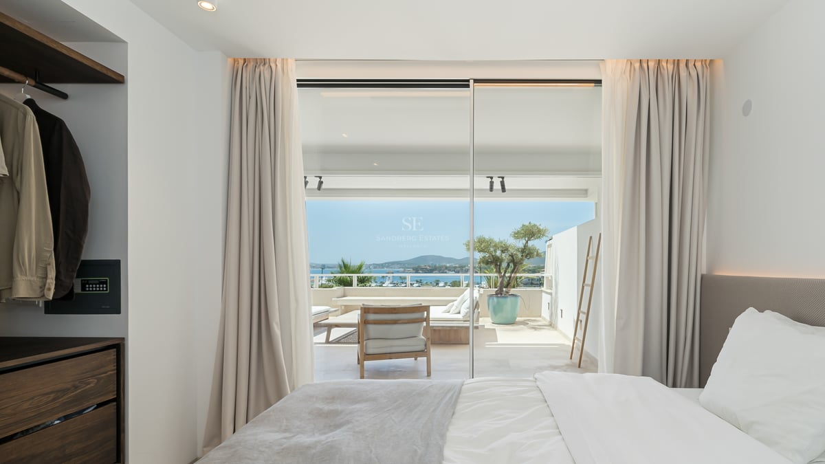 Chambre lumineuse avec baies vitrées s'ouvrant sur une terrasse ensoleillée offrant une vue sur la mer.