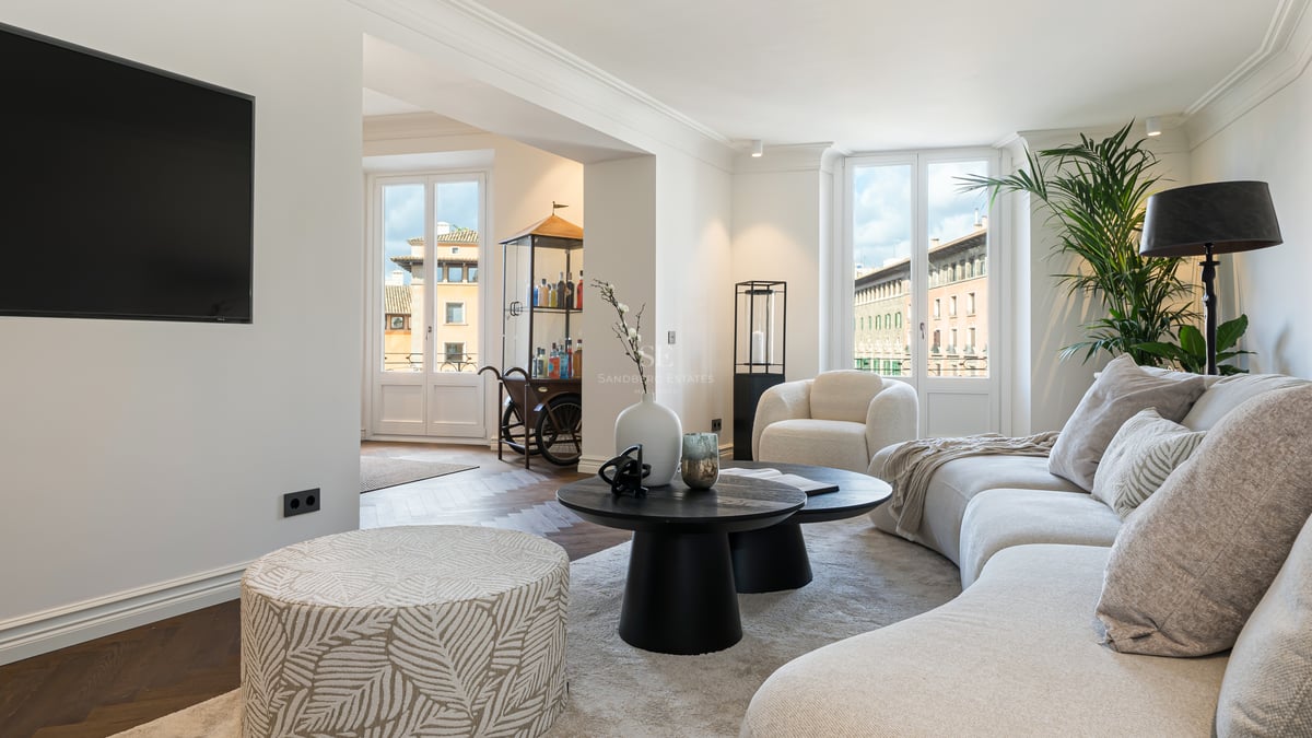 Contemporary living room featuring a curved white sofa, black coffee tables, and large windows overlooking urban buildings.