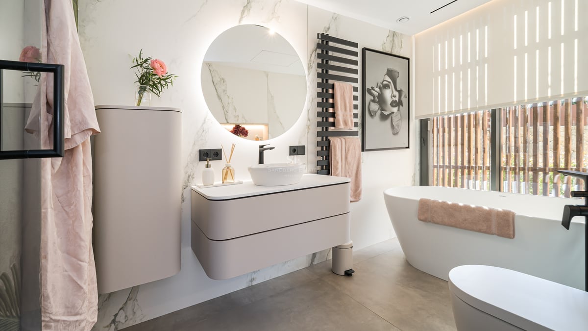 Salle de bain moderne avec miroir rond rétroéclairé, meuble suspendu et baignoire îlot blanche.