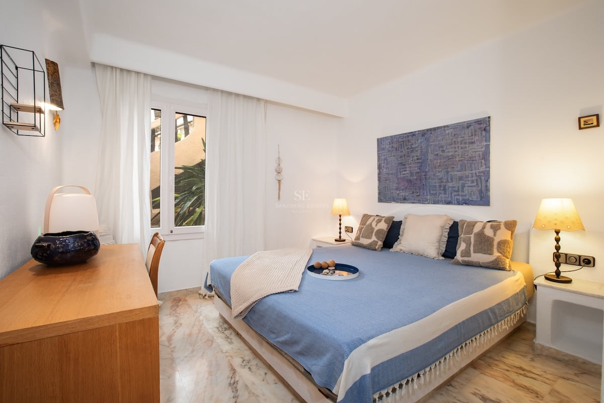 Chambre blanche avec lit bleu, bureau en bois et sol en marbre veiné sous une lumière chaude.