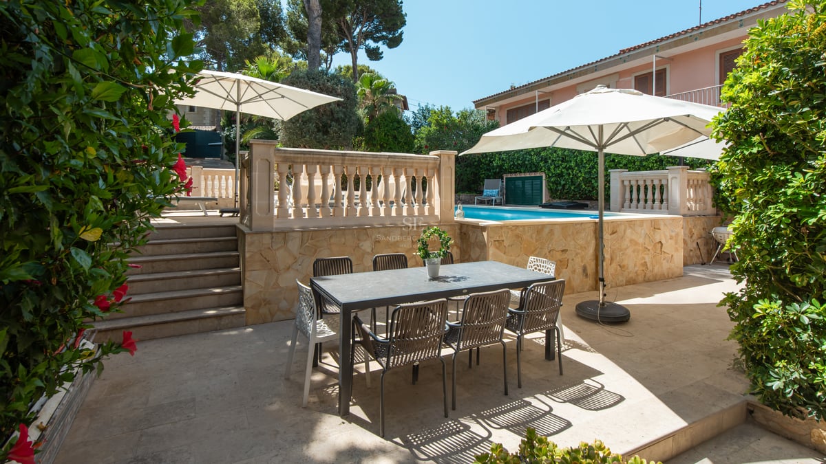 Terrasse avec table à manger sombre et parasols blancs à côté d'une piscine surélevée bleu turquoise.