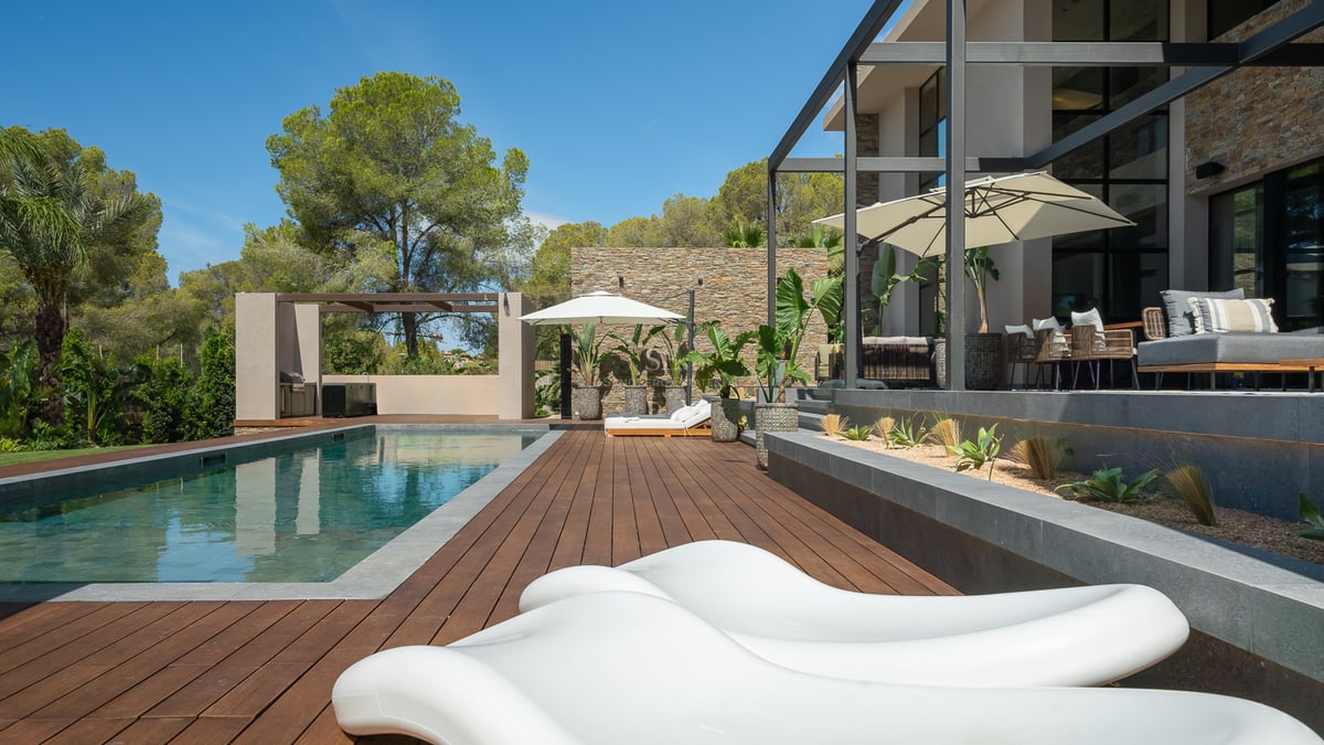 Piscine extérieure de luxe avec terrasse en bois, bains de soleil blancs et murs en pierre sous un ciel bleu.