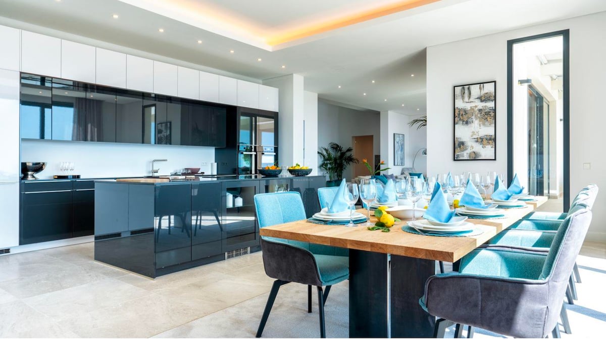 Cuisine moderne haut de gamme avec îlot bleu foncé et table à manger en bois avec chaises turquoise.