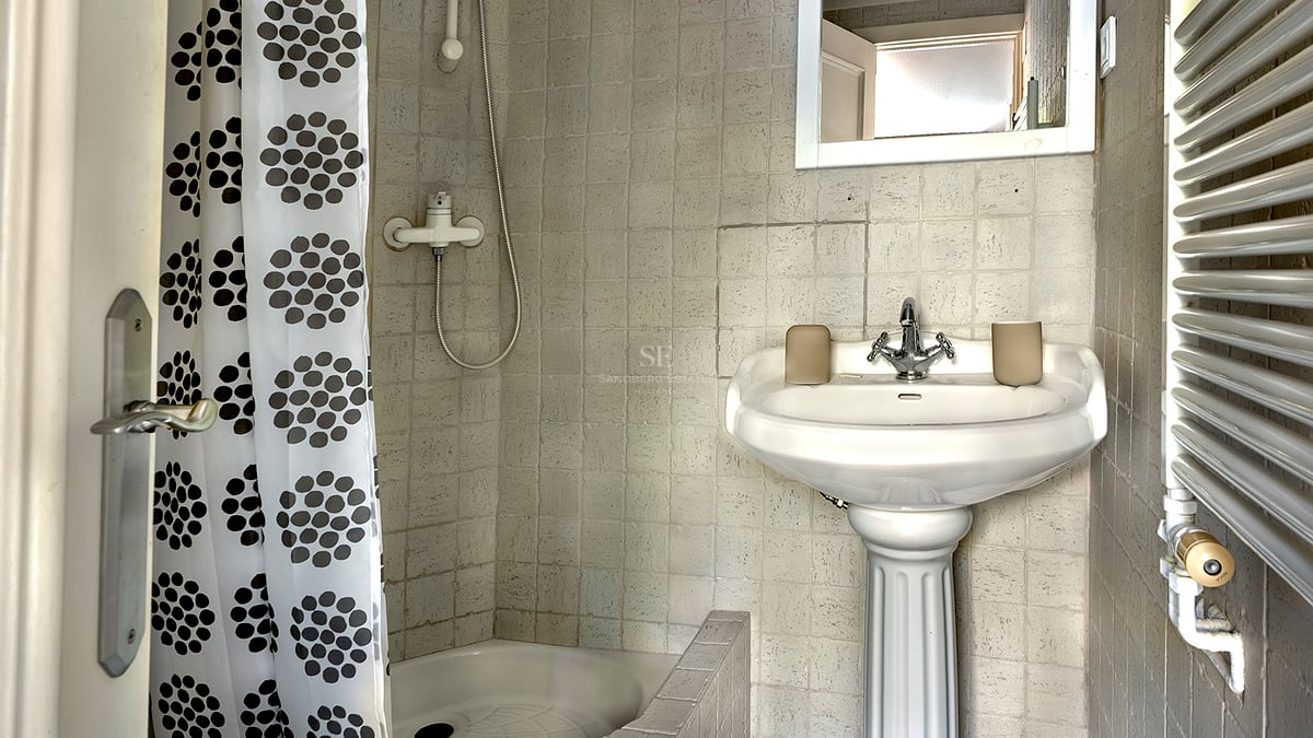 Petite salle de bain avec lavabo sur colonne blanc, murs carrelés et douche avec rideau à pois.