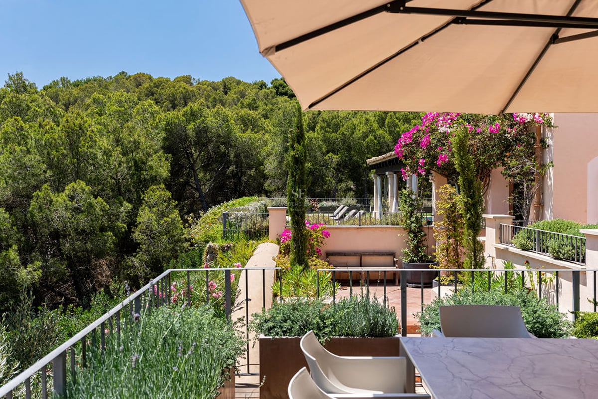Terrasse avec table en marbre et parasol surplombant une forêt de pins luxuriante sous un ciel bleu clair.