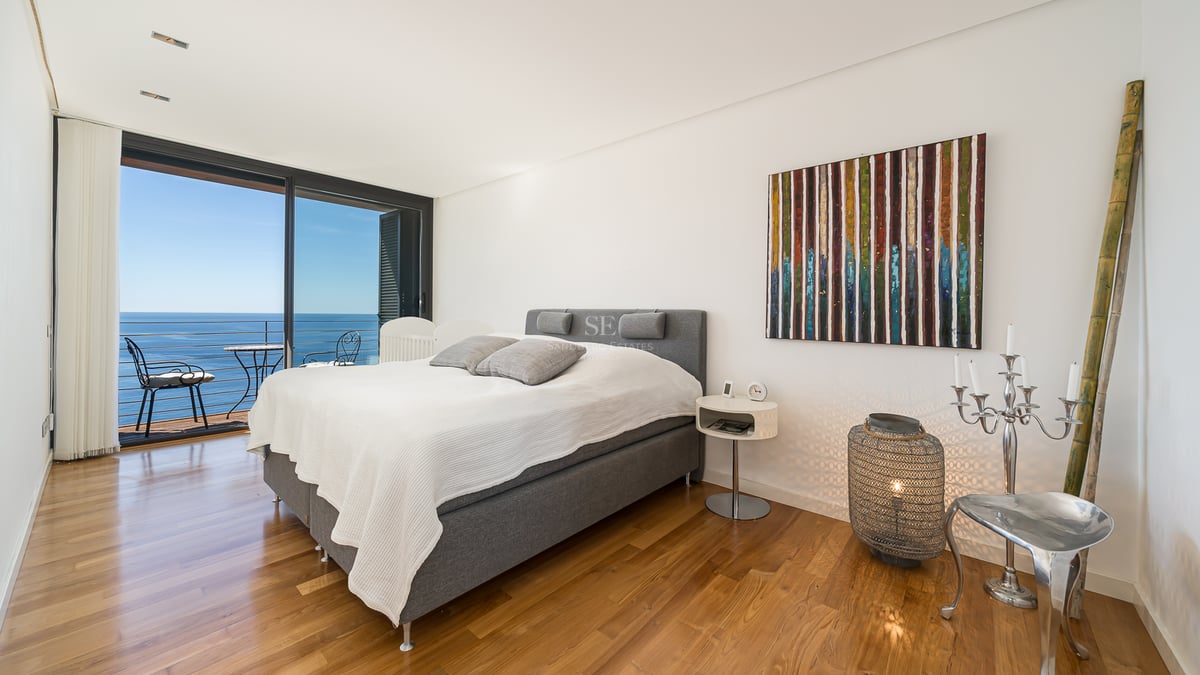 Chambre moderne avec parquet en bois et baies vitrées ouvrant sur un balcon face à la mer.