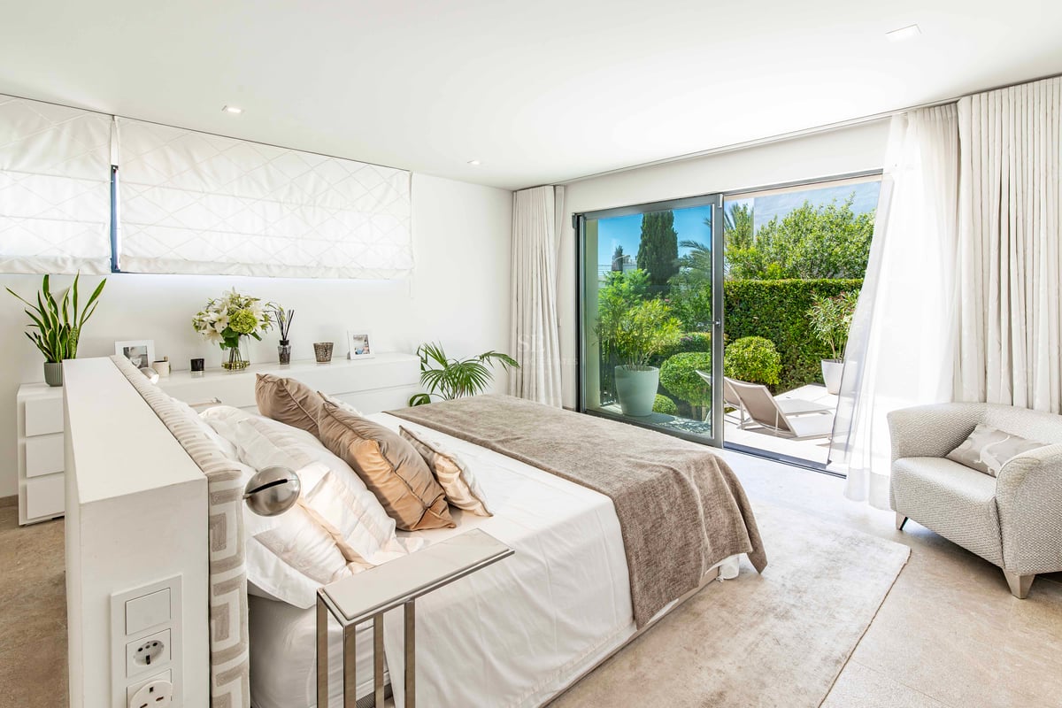 Chambre principale moderne avec baies vitrées coulissantes ouvrant sur une terrasse luxuriante avec chaises longues.