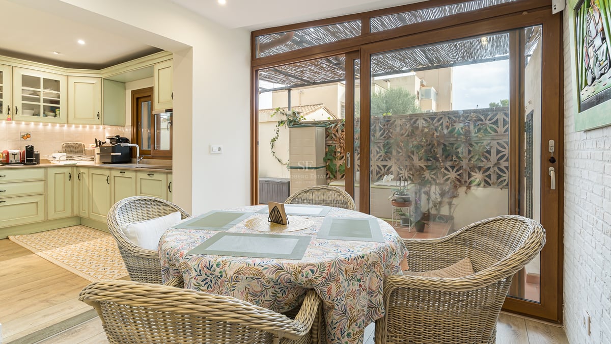 Table à manger avec chaises en osier à côté d'une cuisine vert sauge et de grandes baies vitrées coulissantes.