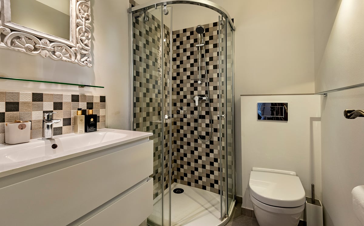 Salle de bain moderne avec une douche en verre, carrelage en damier, lavabo blanc et miroir orné blanc.