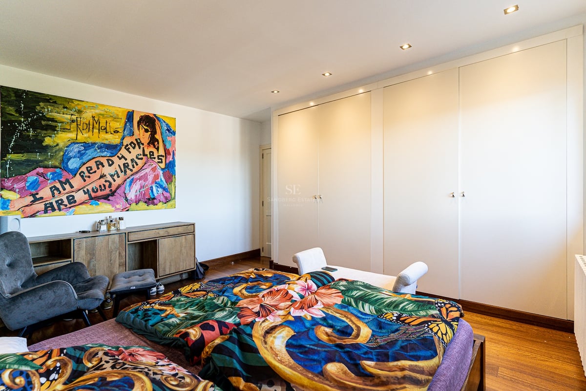 Chambre lumineuse avec placards blancs, parquet en bois, tableau coloré et fauteuil gris.