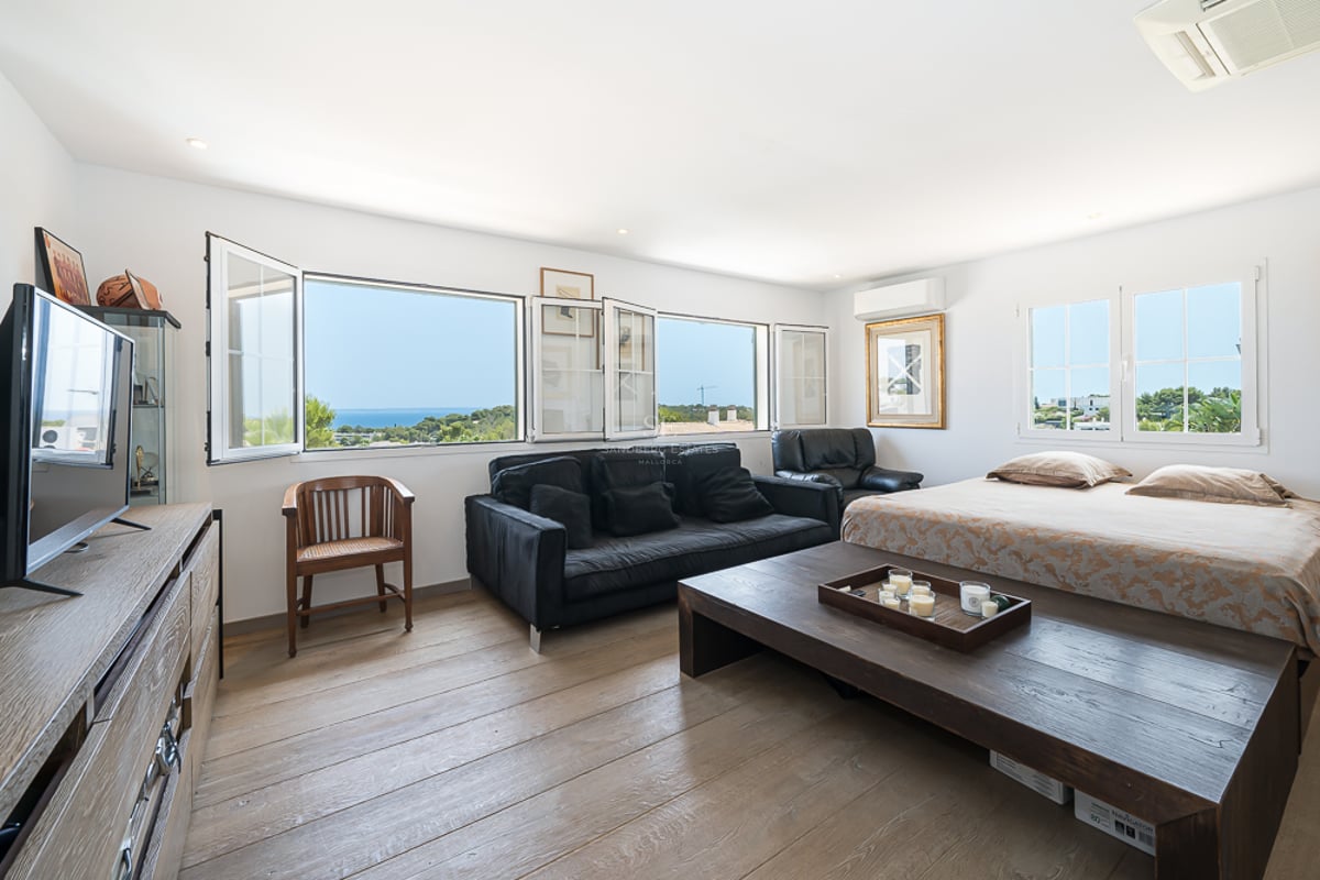 Grande chambre parentale avec parquet en chêne, mobilier en bois sombre et fenêtres donnant sur la mer Méditerranée.