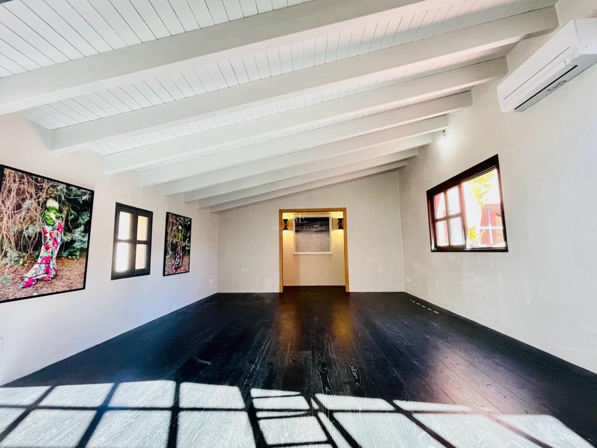 Pièce minimaliste avec parquet foncé, plafonds à poutres blanches et œuvres d'art modernes sous la lumière du jour.