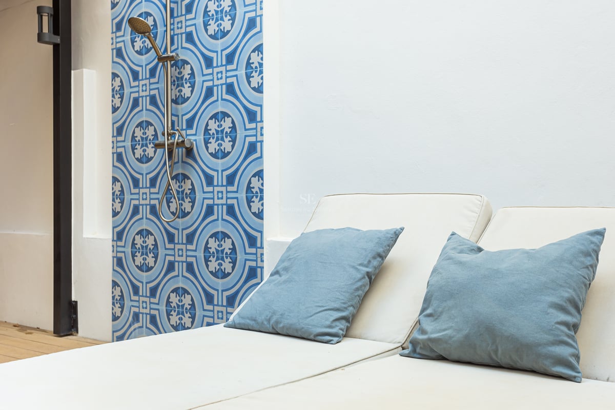 Chaise longue avec coussins bleus à côté d'un mur en carreaux bleus et d'une douche extérieure moderne.
