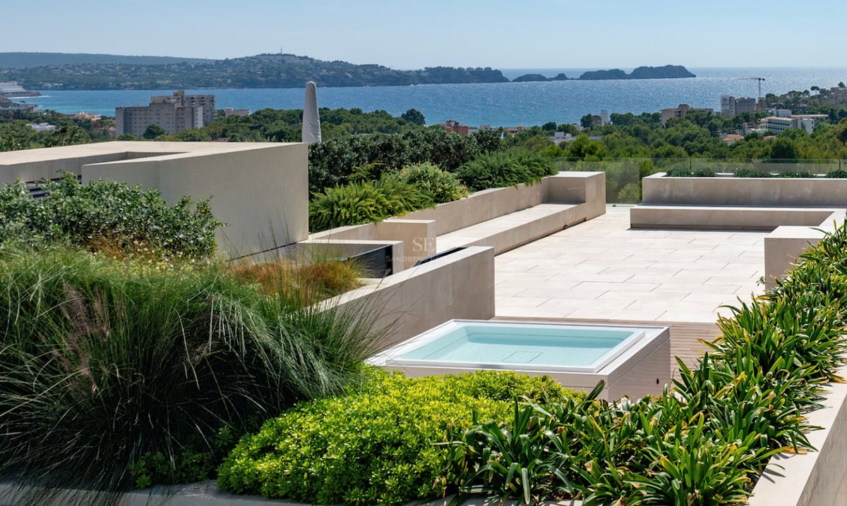 Terrasse de toit moderne avec une petite piscine, pavage en pierre, jardinières verdoyantes et vue sur la mer.