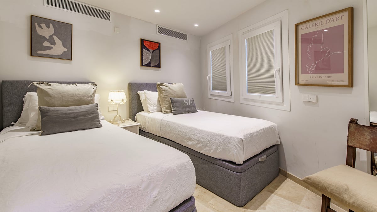 Chambre avec deux lits simples, têtes de lit grises, draps blancs et art mural contemporain.