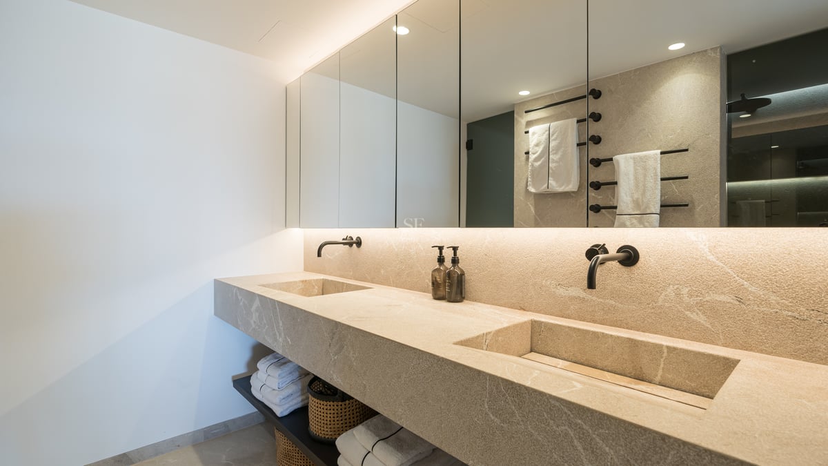 Salle de bain de luxe avec double vasque intégrée en pierre, miroirs rétroéclairés et robinetterie noire mate.