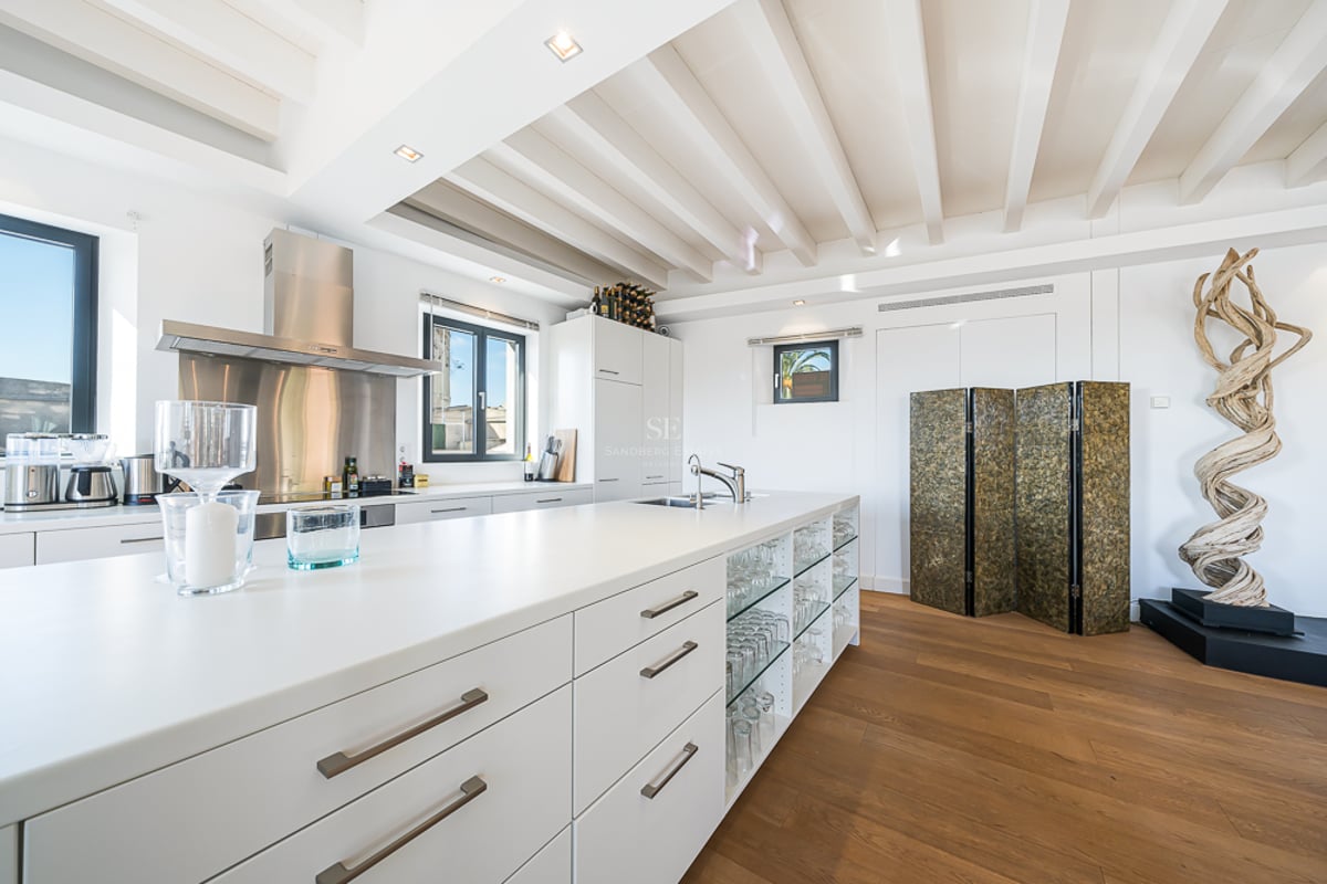 Cuisine blanche moderne avec grand îlot, parquet, poutres au plafond et une sculpture décorative en bois.