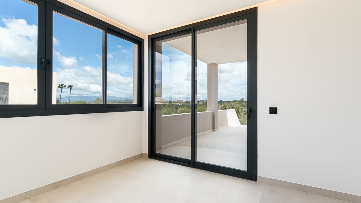 Pièce lumineuse avec grandes baies vitrées coulissantes à cadre noir ouvrant sur une terrasse privée ensoleillée.
