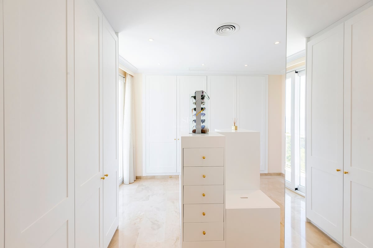 Dressing blanc moderne avec placards intégrés, îlot central et sol en marbre sous une lumière naturelle.