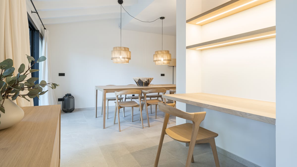 Salle à manger lumineuse avec table en chêne, bureau intégré avec étagères LED et sol en grès cérame.