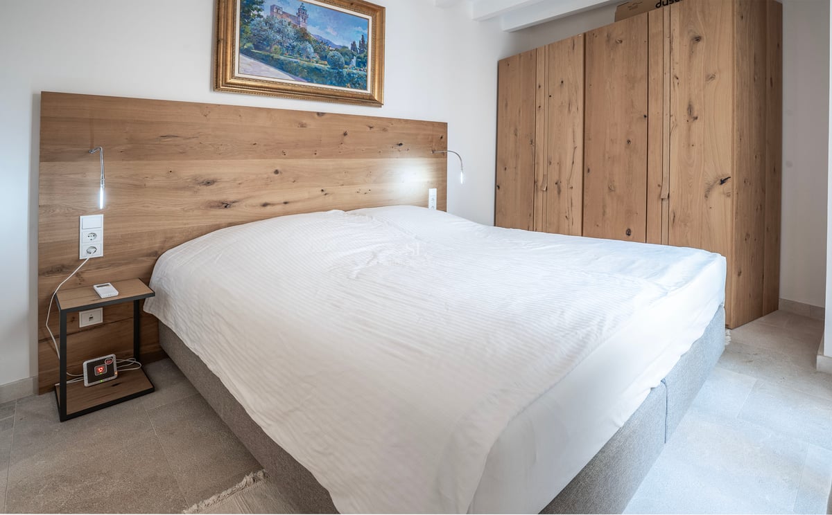 Chambre moderne avec grand lit, tête de lit et armoire en bois clair et un tableau classique.
