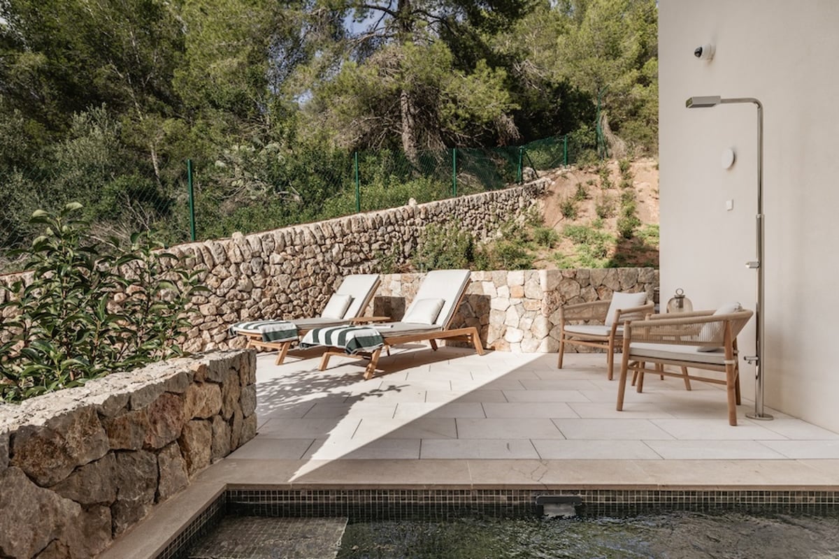 Terrasse moderne en pierre avec bains de soleil, douche extérieure en métal et vue sur une forêt dense.
