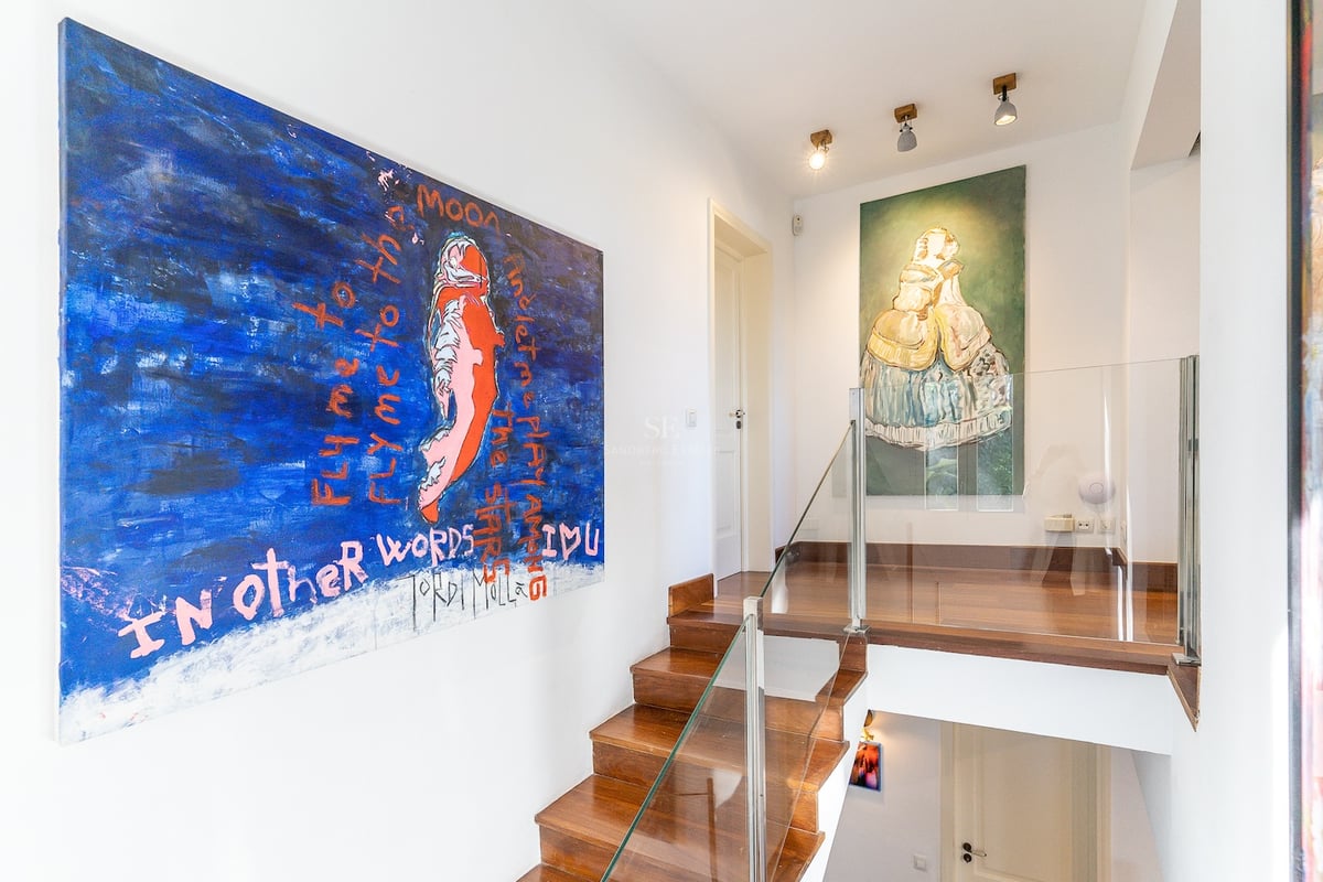 Escalier moderne en bois avec garde-corps en verre et grands tableaux abstraits sur murs blancs.