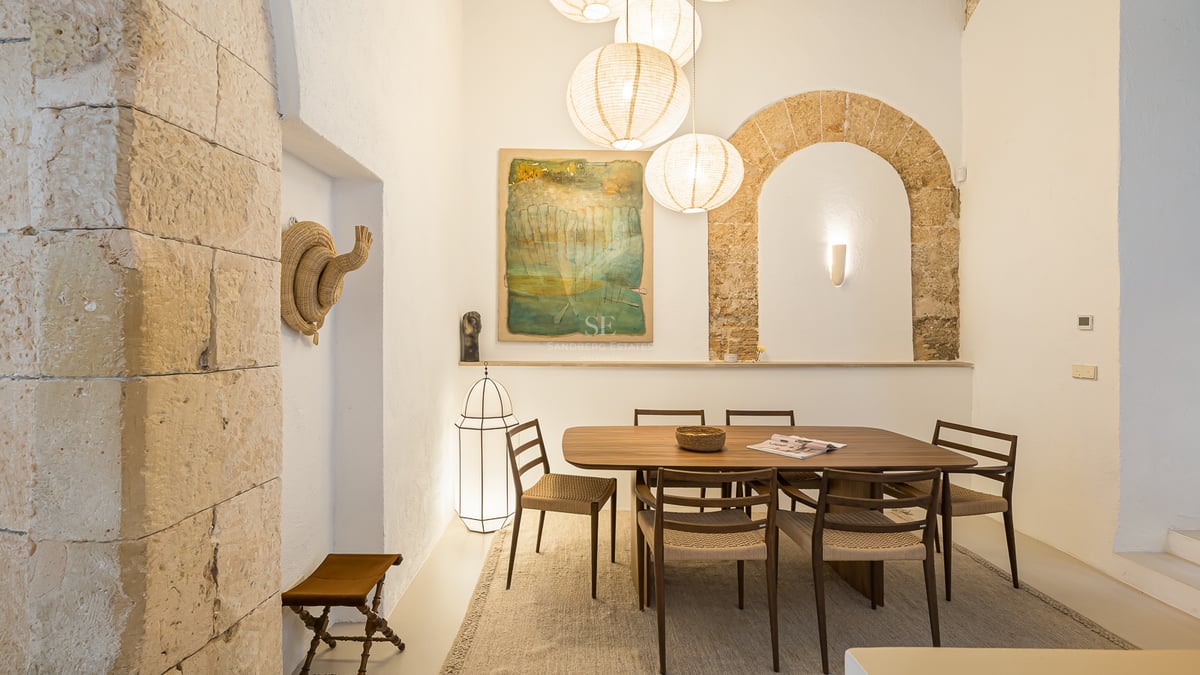 Table à manger moderne en bois et chaises sous des lanternes en papier dans une pièce avec une arche en pierre apparente.