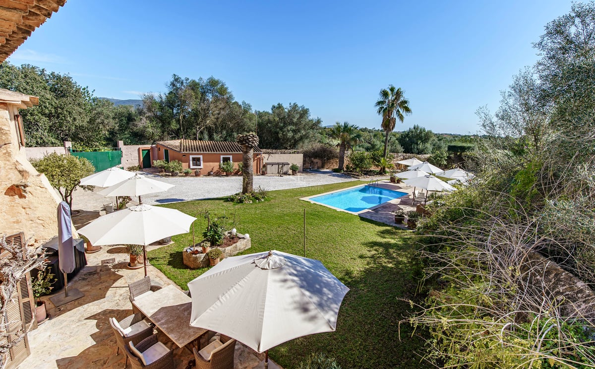 Piscine rectangulaire entourée d'une pelouse verte, de parasols et d'une terrasse en pierre dans un domaine méditerranéen.