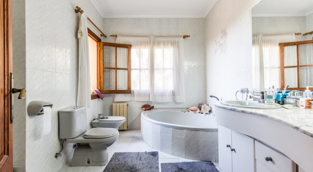 Salle de bain spacieuse avec une grande baignoire d'angle, un meuble-lavabo en marbre, des toilettes, un bidet et des fenêtres en bois.