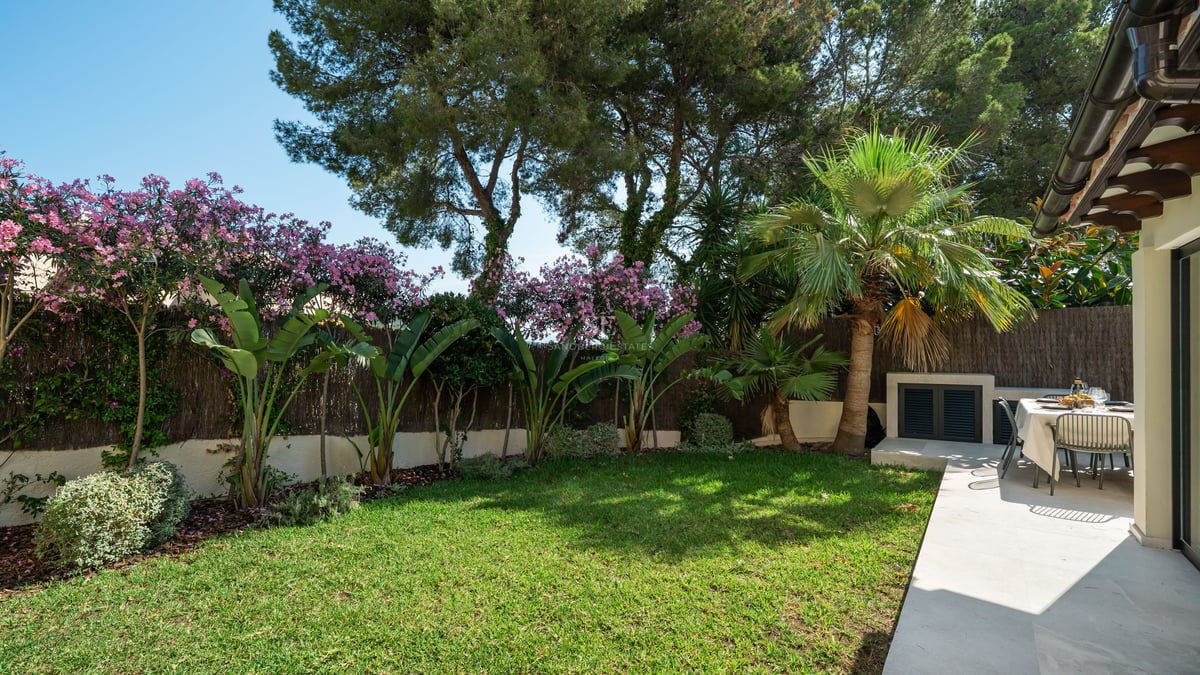 Jardin privé avec pelouse impeccable, plantes tropicales et terrasse en pierre avec table à manger ensoleillée.