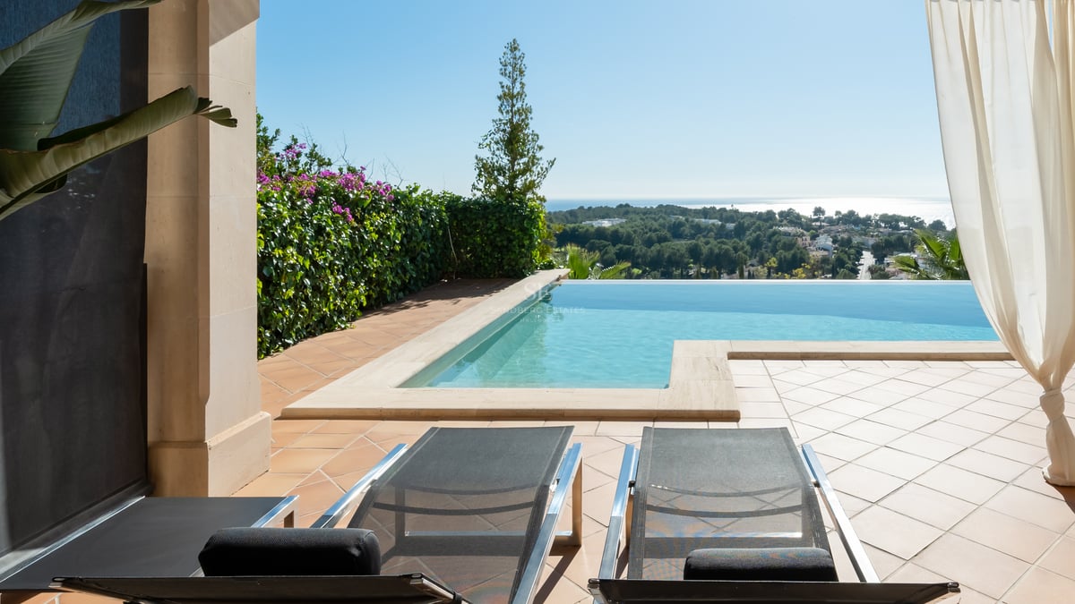 Piscine à débordement sur terrasse en terre cuite avec transats dominant une vallée verdoyante face à la mer.