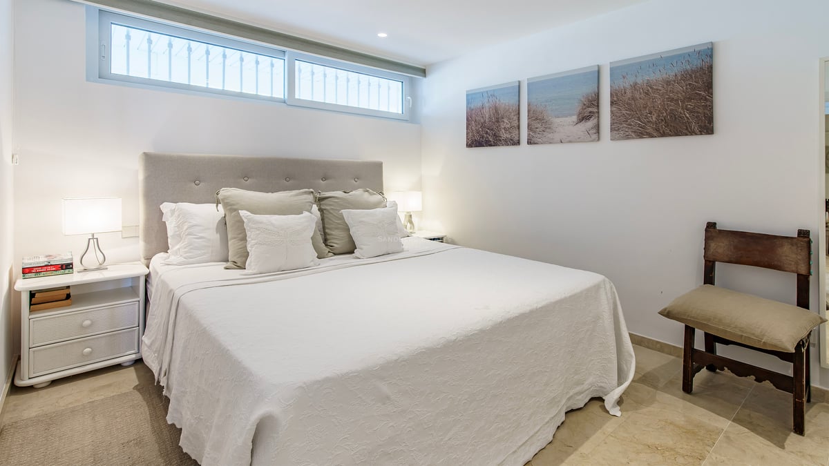 Chambre lumineuse avec grand lit, tête de lit grise, literie blanche et triptyque de paysages côtiers.