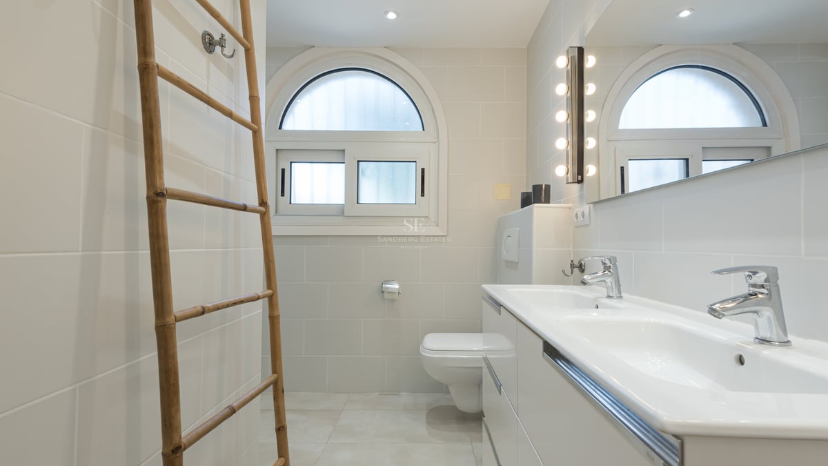 Salle de bain contemporaine avec double vasque blanche, fenêtre en arche et échelle décorative en bambou.