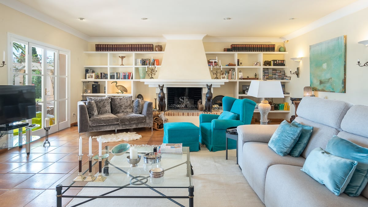Bright living room featuring terracotta floors, gray sofas, a teal armchair, central fireplace, and built-in shelving.