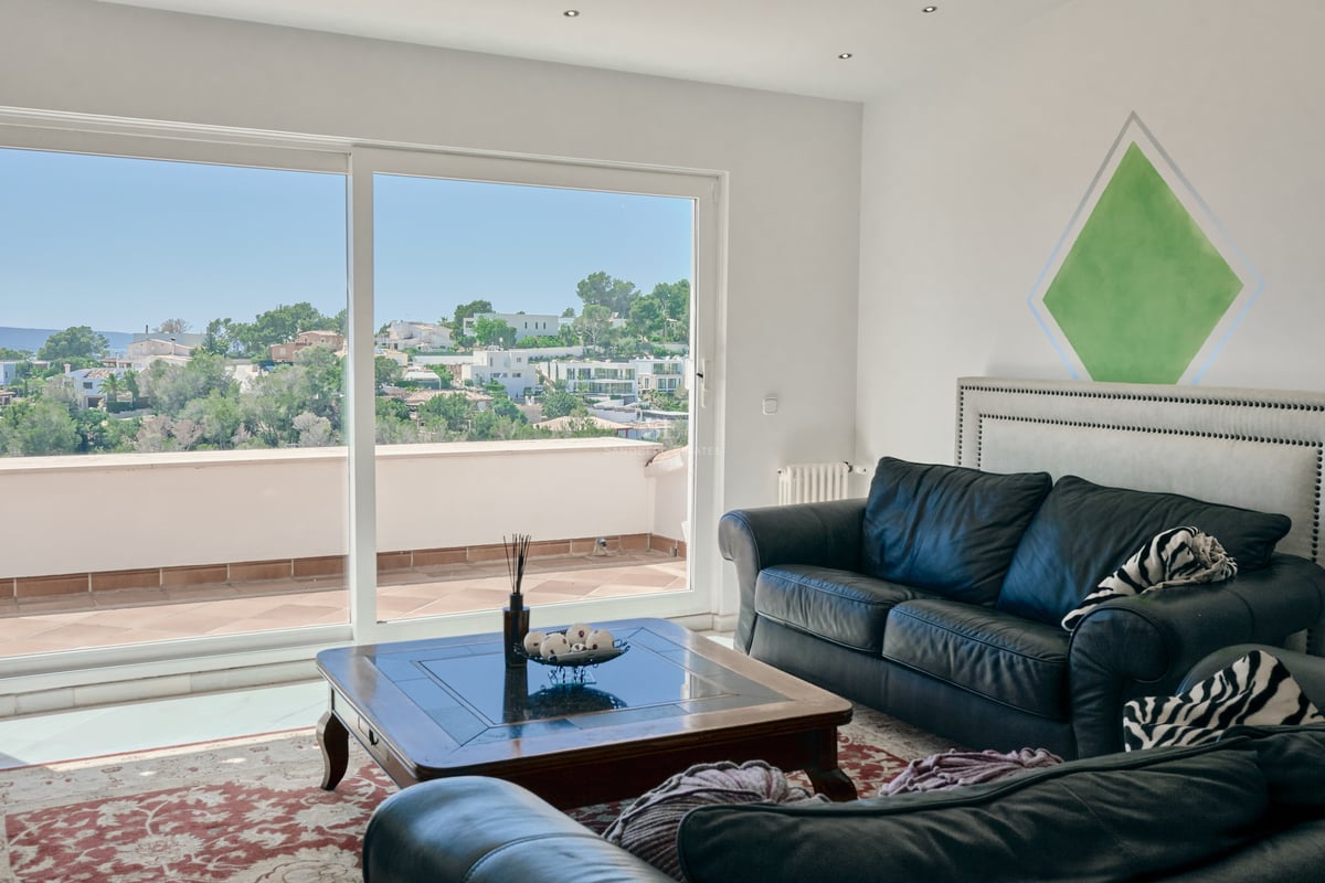 Salon moderne avec canapés en cuir noir et grandes baies vitrées s'ouvrant sur une terrasse surplombant les collines.