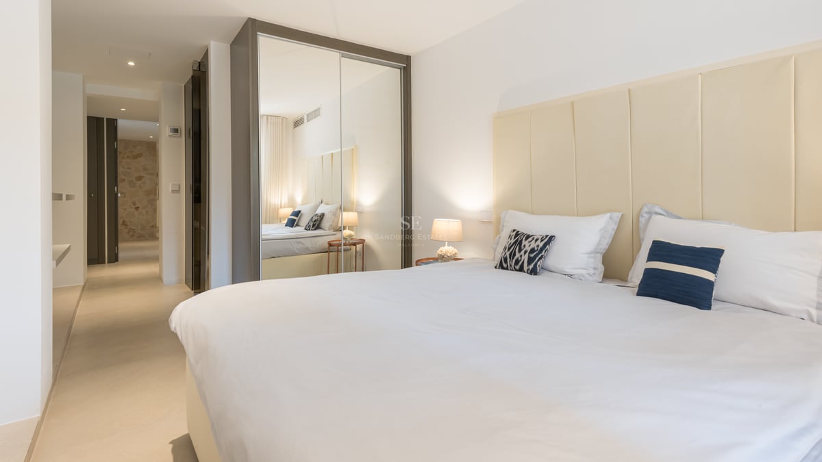 Chambre lumineuse avec un grand lit, tête de lit en tissu crème et placards à portes miroirs.