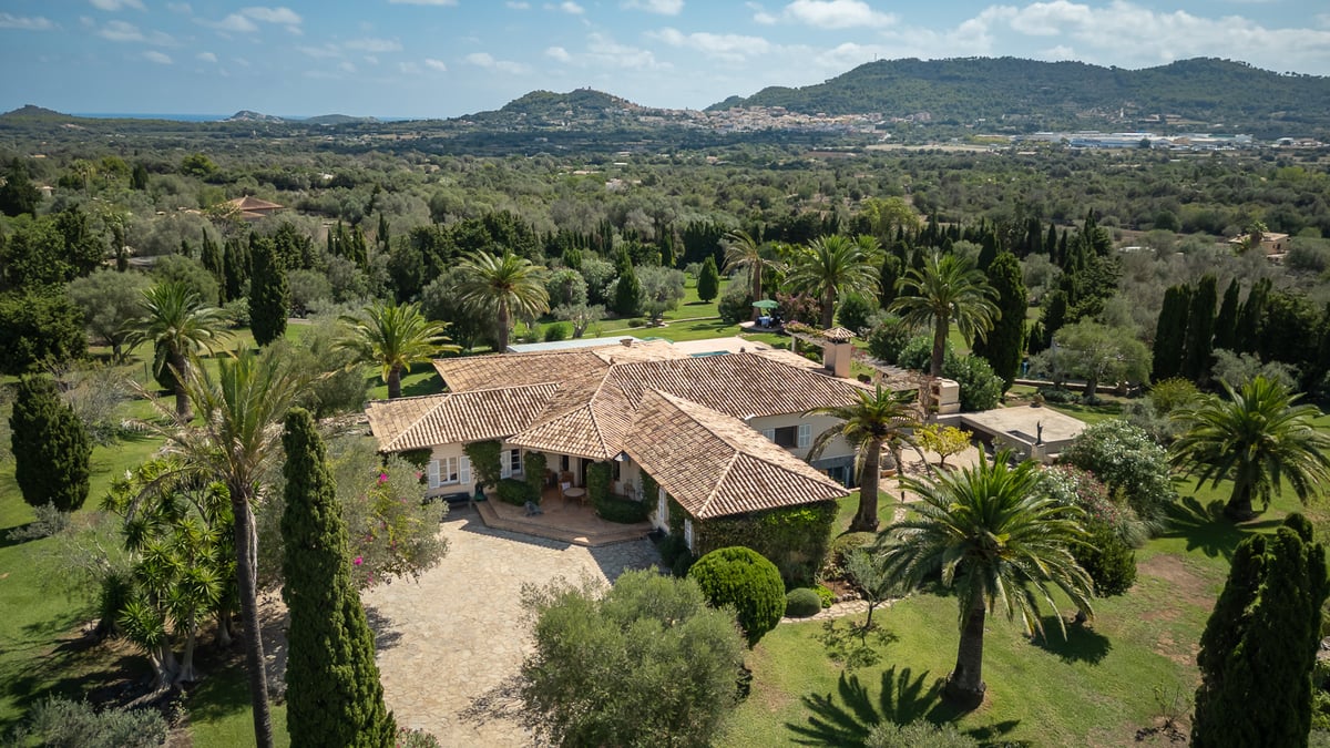 Aerial view of a large Mediterranean villa with terracotta roofs surrounded by mature palms and lush greenery.