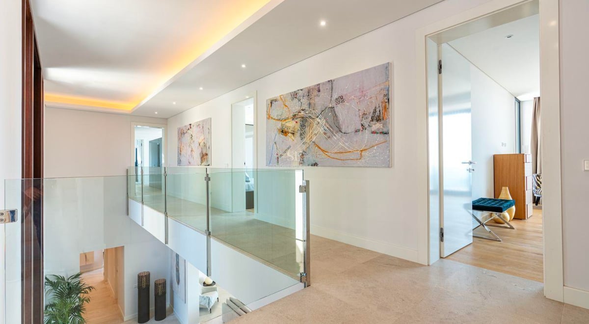 Couloir moderne avec balustrades en verre, art abstrait et sols en pierre surplombant l'étage inférieur.