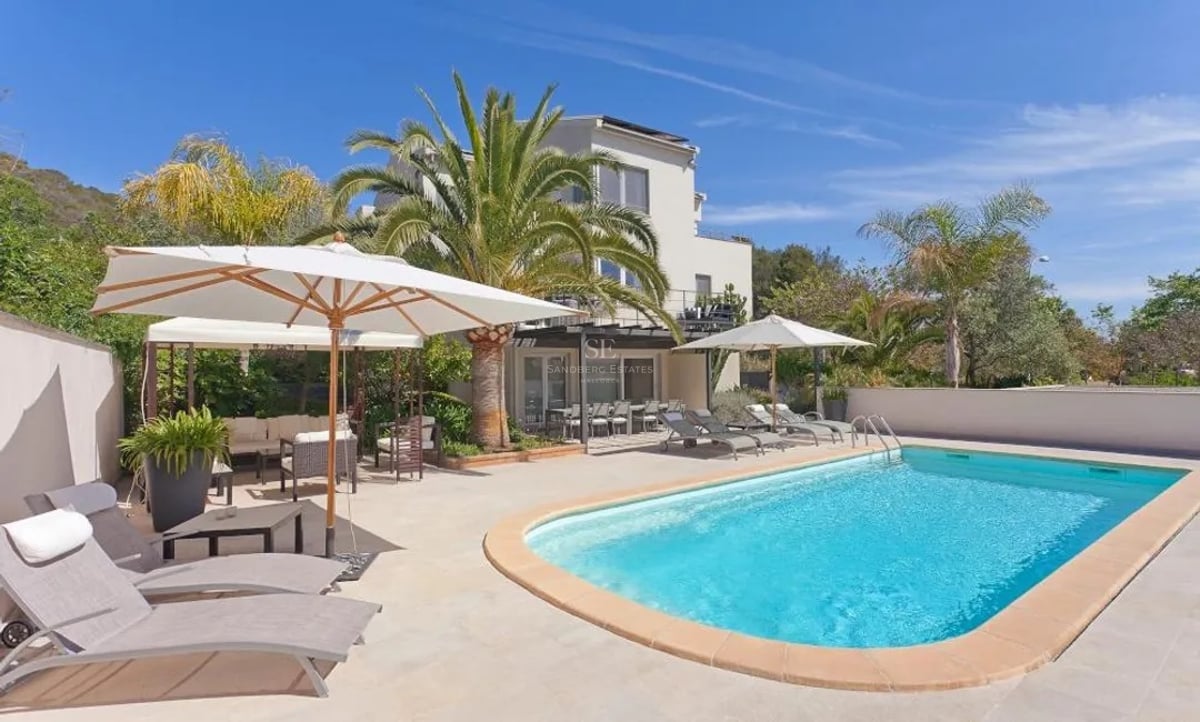 Piscine de luxe aux eaux turquoise, terrasse en pierre beige, chaises longues et palmiers sous un ciel bleu.