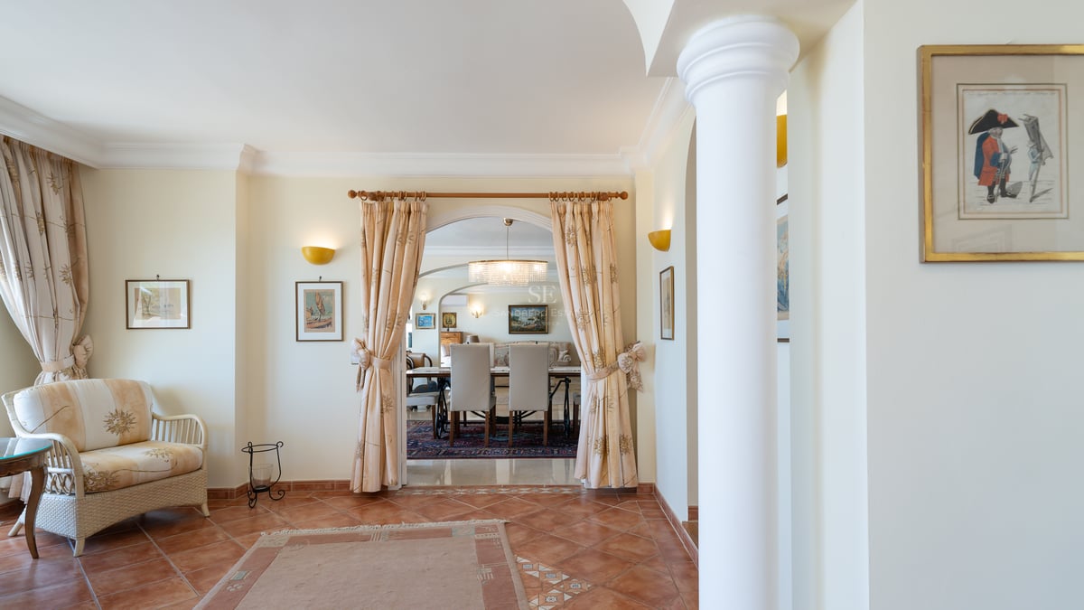 Intérieur avec sols en terre cuite, arche avec rideaux, colonne blanche et vue sur la salle à manger d'une villa.