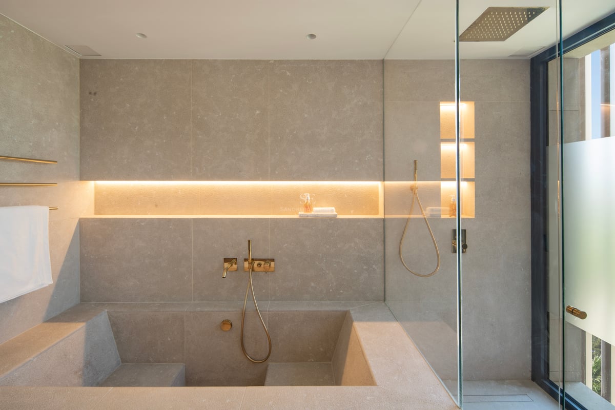 Salle de bains de luxe minimaliste avec baignoire en pierre sur mesure, douche à l'italienne et robinetterie dorée.