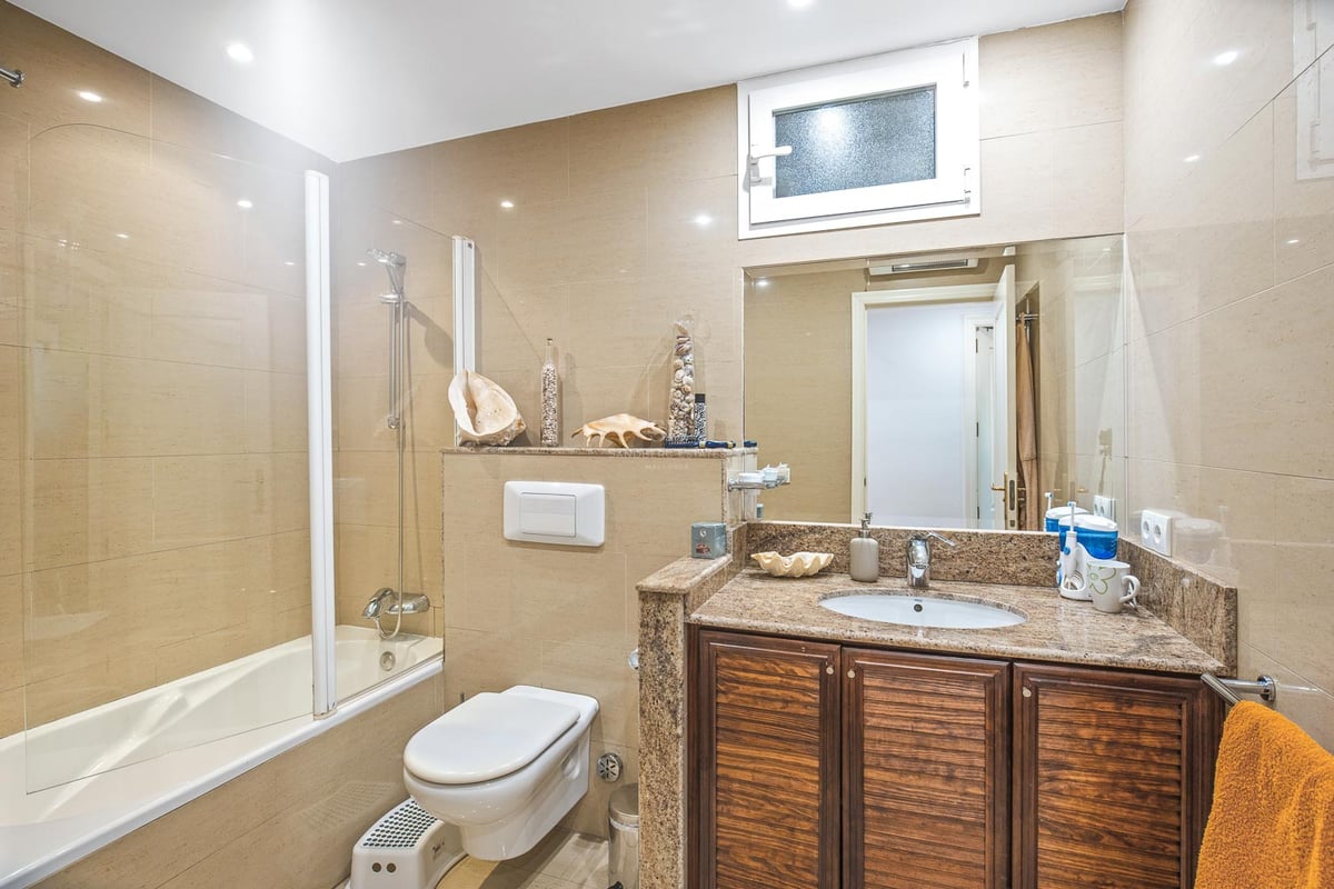 Salle de bain avec baignoire, paroi en verre, meuble en bois sombre, plan en granit et carrelage ton sable.