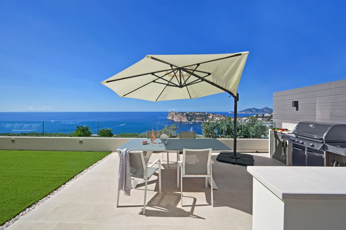 Terrasse extérieure avec table à manger, parasol, barbecue et vue imprenable sur l'océan sous un ciel bleu clair.