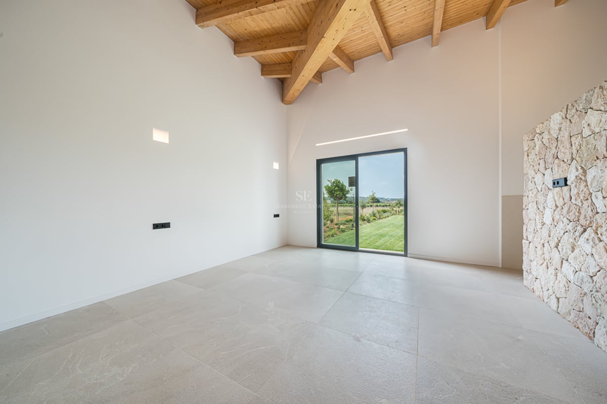 Pièce moderne vide avec haut plafond en bois, mur en pierre naturelle et baie vitrée ouvrant sur un jardin.