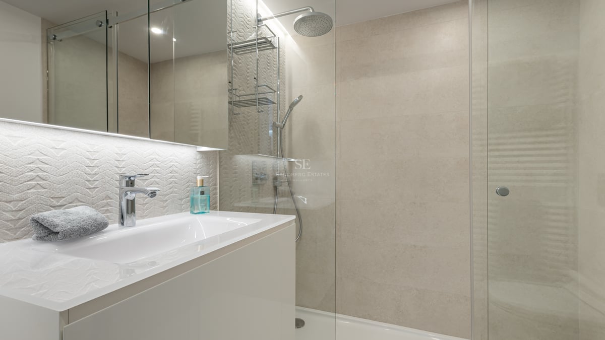 Salle de bain contemporaine avec douche vitrée, vanité blanche et carrelage mural texturé crème.