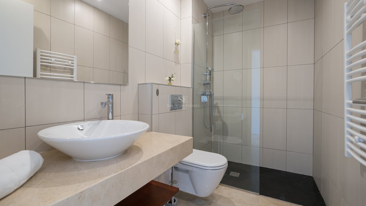 Salle de bain moderne avec carrelage beige, plan en marbre, vasque à poser et douche avec paroi vitrée.