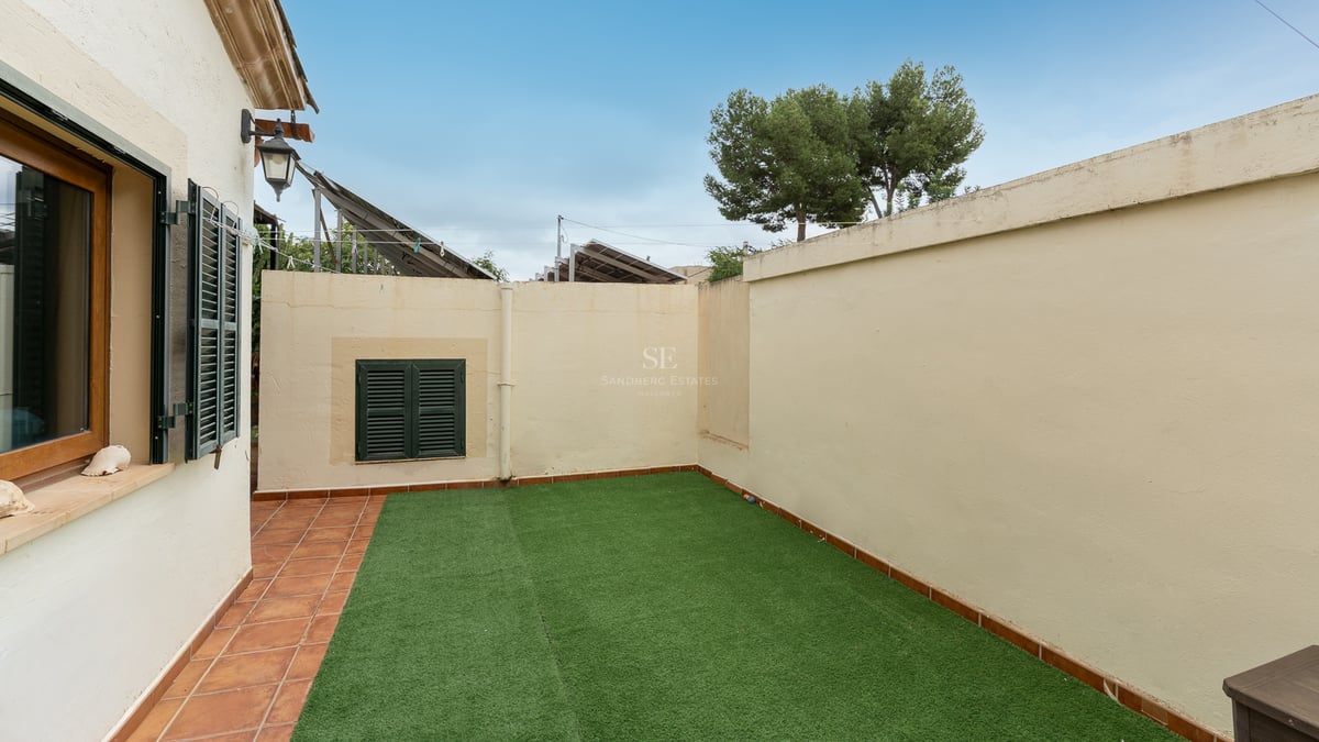 Petit jardin clos avec gazon artificiel et bordure en terre cuite sous un ciel bleu.