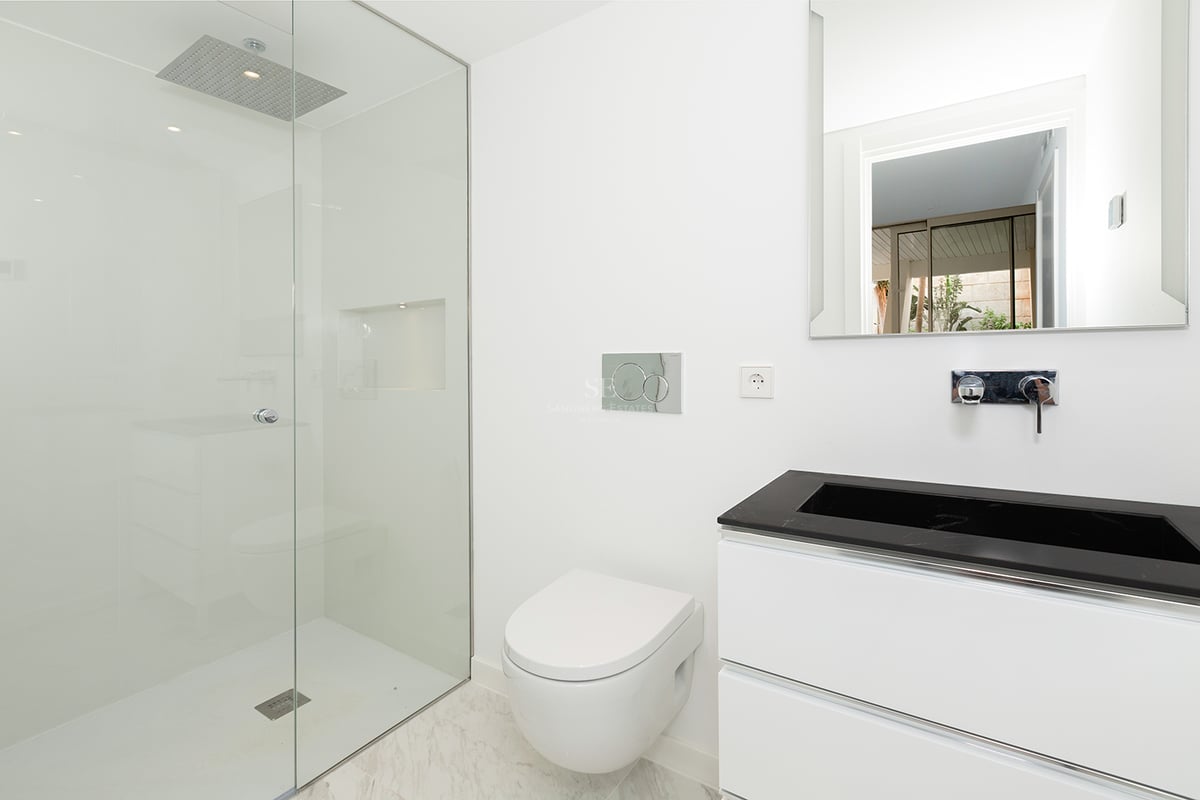 Salle de bain lumineuse et minimaliste avec douche en verre, toilettes suspendues et meuble vasque noir et blanc.