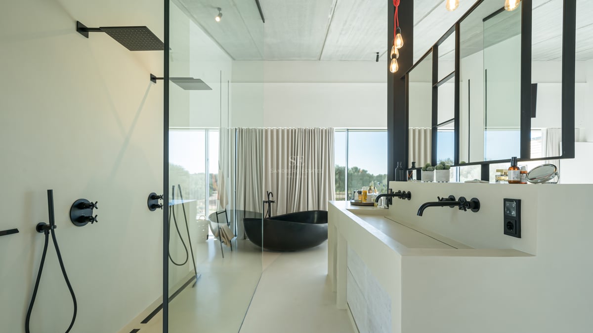 Salle de bains minimaliste avec baignoire îlot noire, double vasque blanche et grandes baies vitrées.
